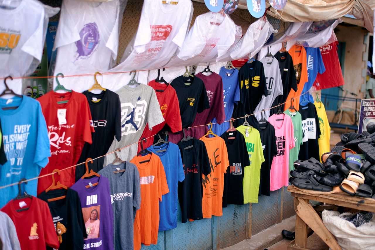 Vibrant collection of T-shirts and shoes on display at an outdoor market stall in Jos, Nigeria.