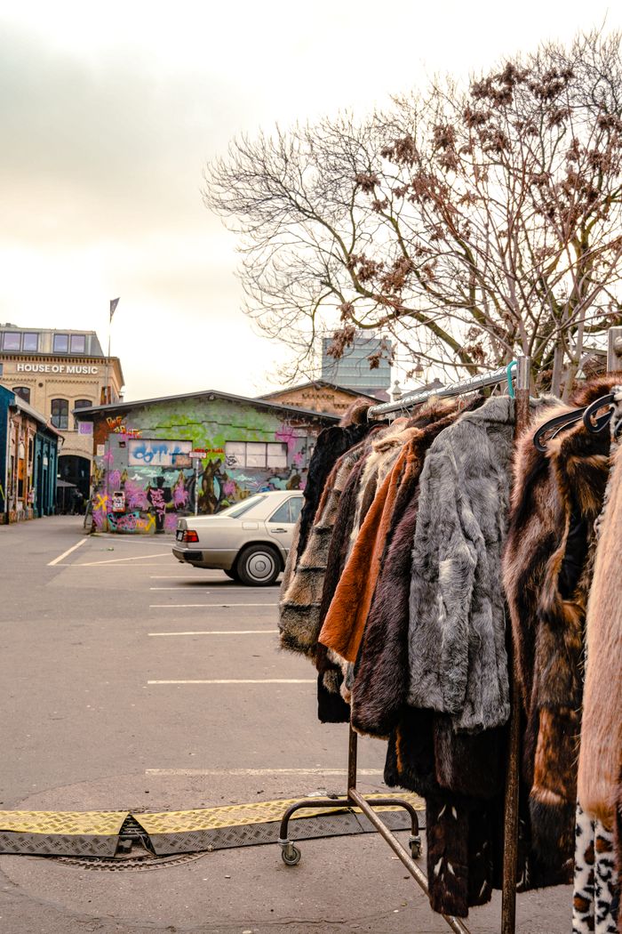 A rack of fur coats in a vibrant, graffiti-adorned urban alley setting.